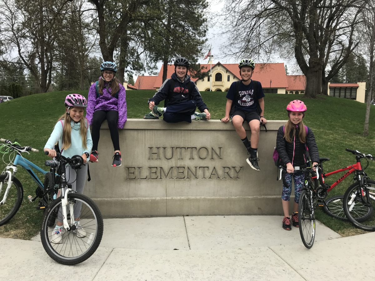 Students sitting on Hutton Elementary School sign with bikes next to them. 
