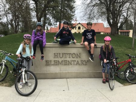 Students sitting on Hutton Elementary School sign with bikes next to them.