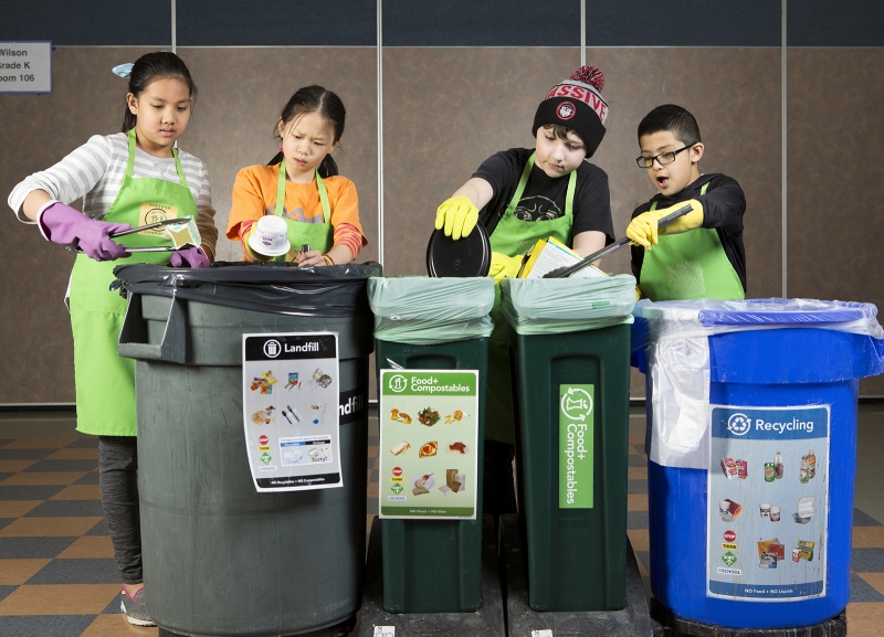 Four elementary students sorting food waste into multi-colored bins