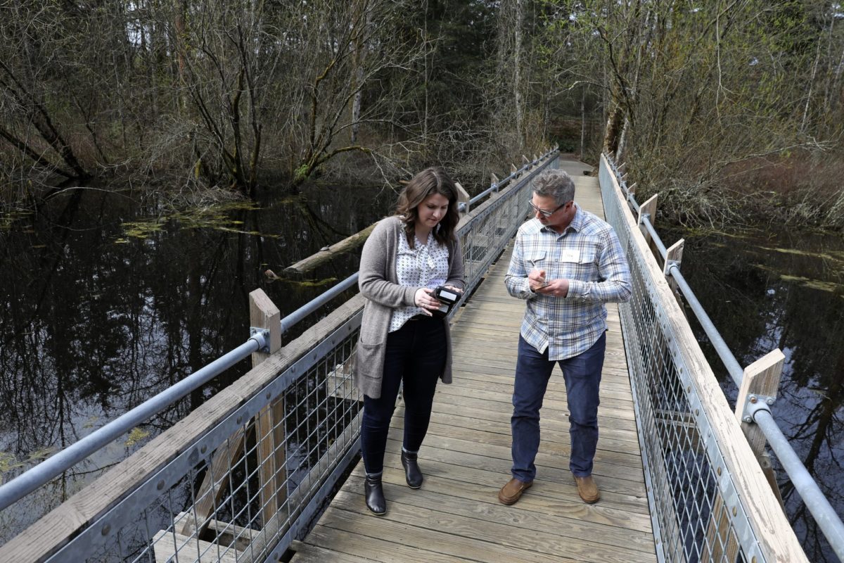 Two educators stand on a bridge look at an air quality meter as part of a Washington Green Schools training.