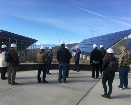 A group of educators in hard hats look out onto a field of solar panels and wind turbines at the Wild Horse Wind and Solar Facility in Yakima.