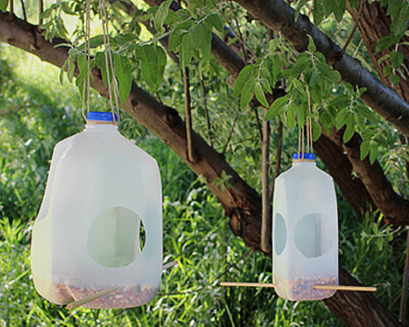 Two plastic milk carton bird feeders hang in a tree.