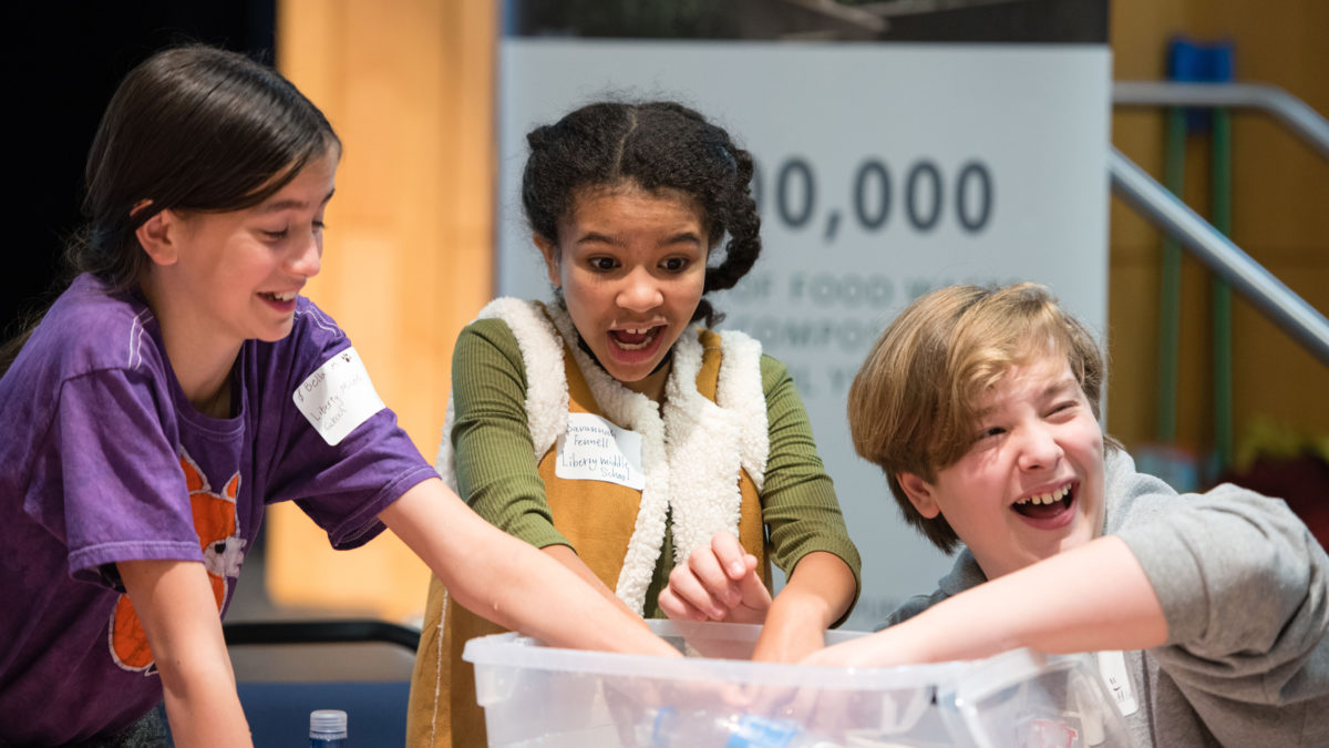 Three students reach their hands into a plastic bin.