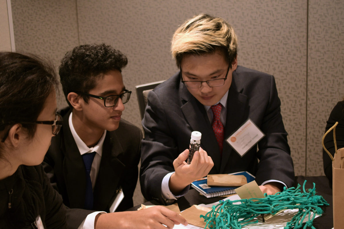 3 high school students look at a small vial of microplastic bits at the Clark County High School Summit