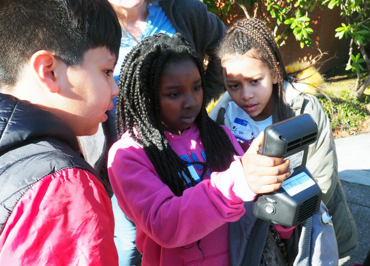 3 students look at an air quality meter.