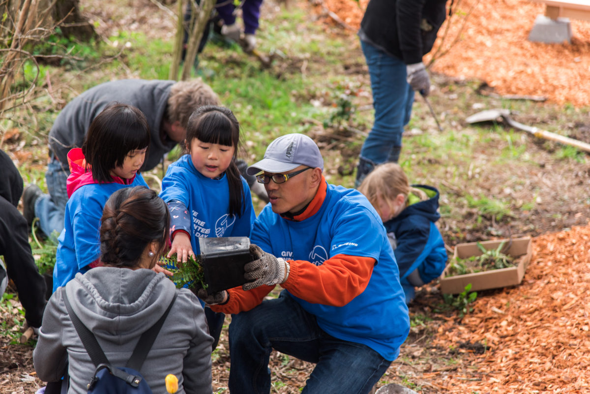 2 adults and 2 children pull a plant out of its pot at a volunteer planting event