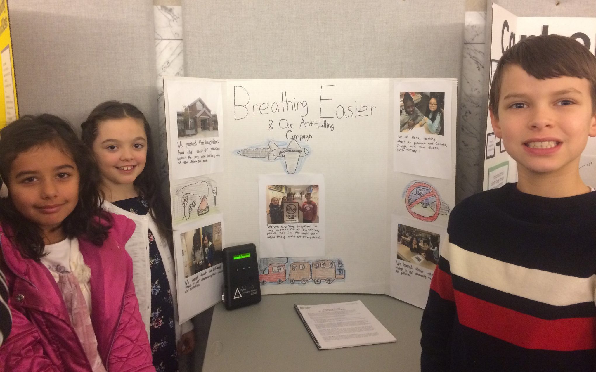 Three elementary students stand next to their tri-panel poster presentation on their Breathing Easier Anti-idling campaign.