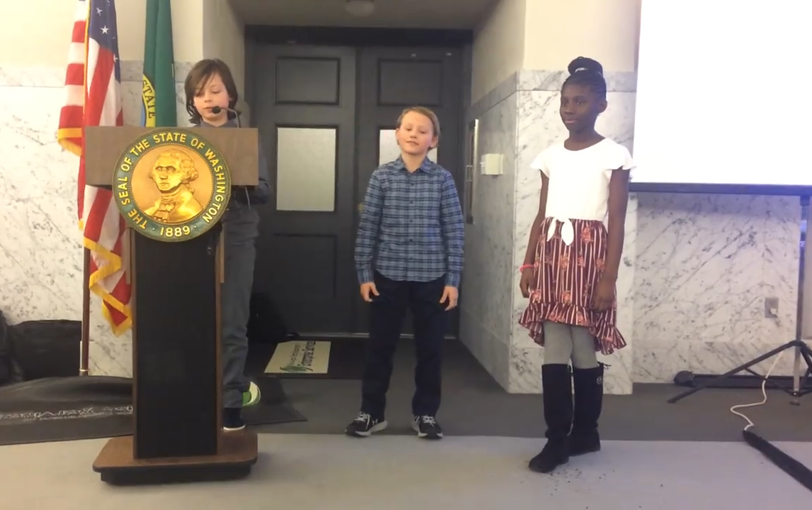 Three students on stage at the state Capitol in Olympia presenting their anti-idling campaign. 