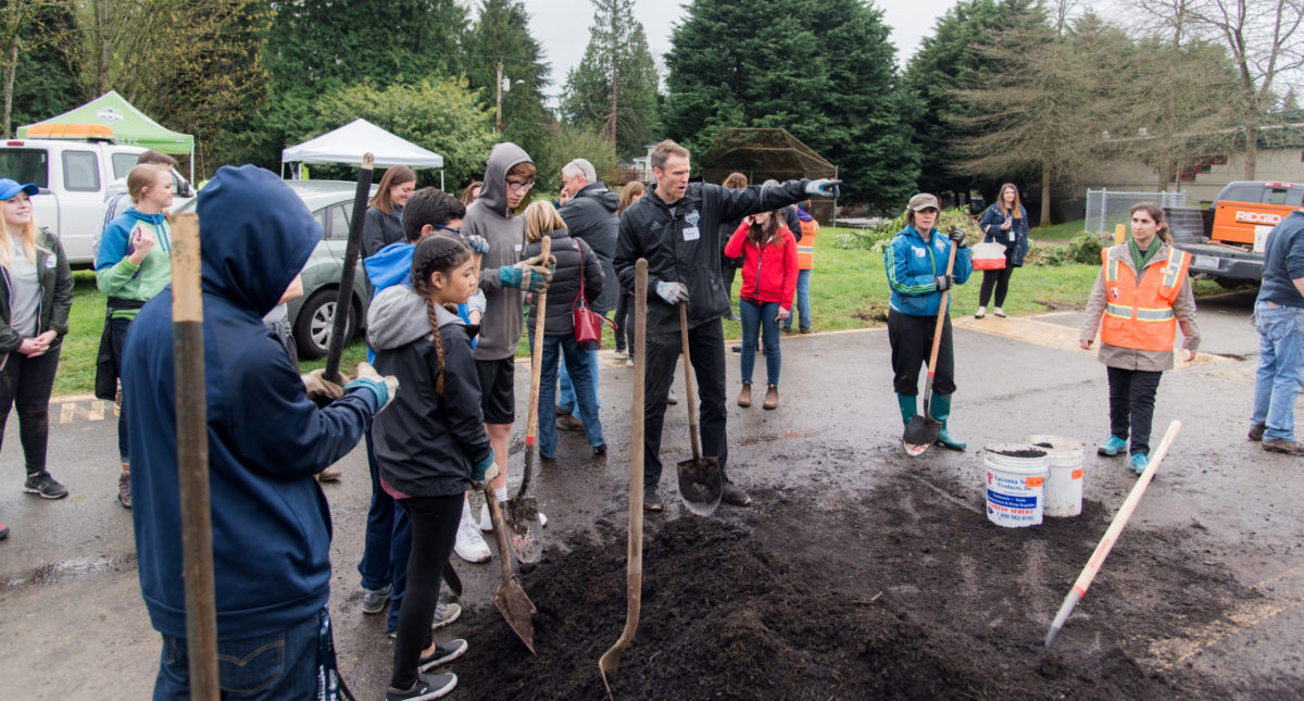 A group of students and volunteers gather around a pile of soil in preparation for spreading in a newly installed rain garden.