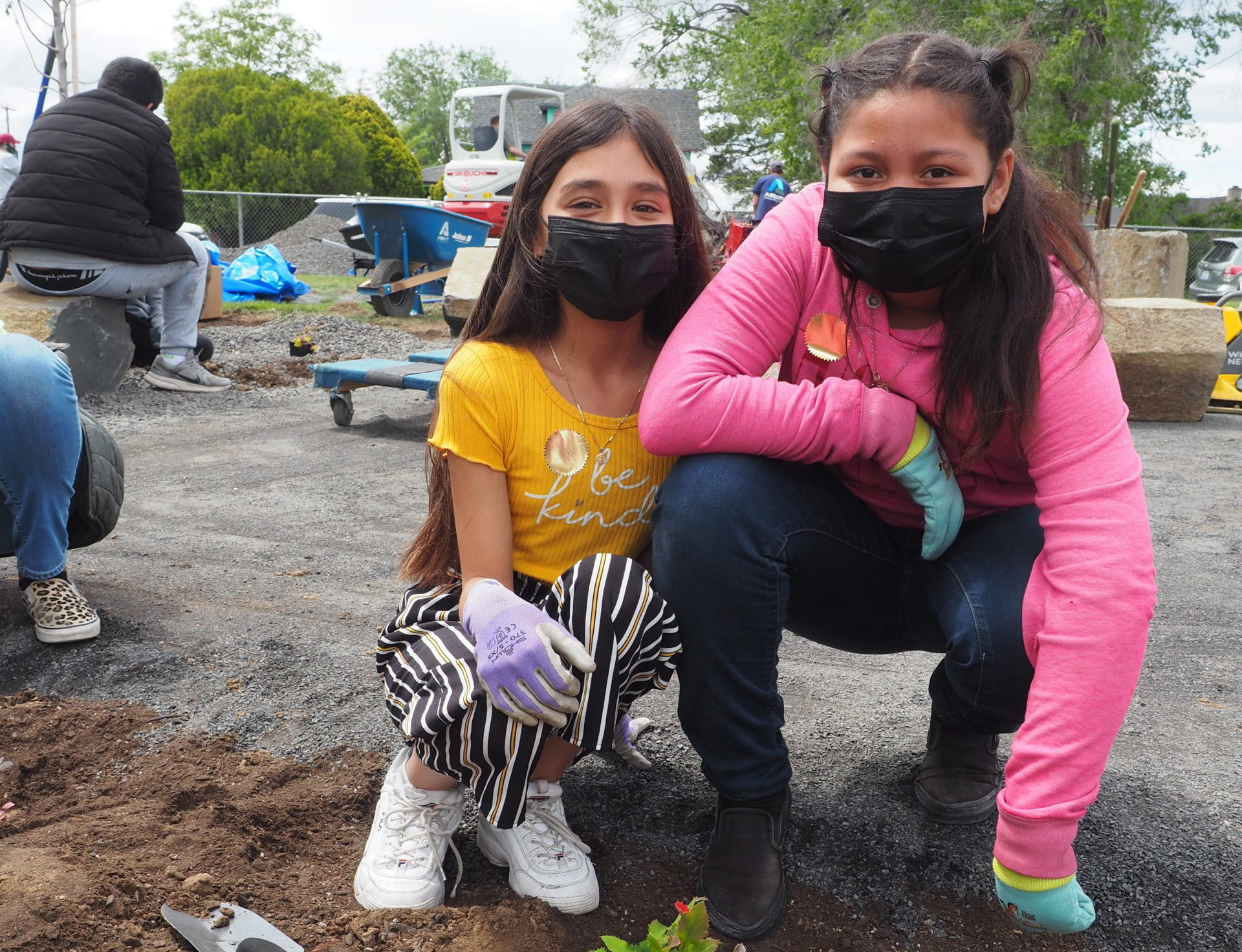 2 students pose for the camera after planing plants in their new drought tolerant garden. Even though they are wearing masks, they are smiling beneath them.