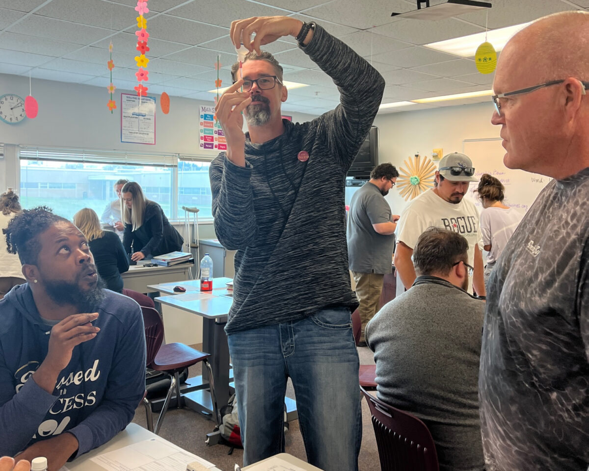 A group of educators look on as another educator holds up a test tube and test strip during water quality testing at a recent Stormwater Challenge teacher training. 