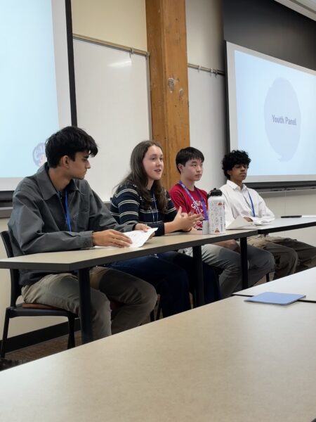4 students sit at a table and look out into a crowd