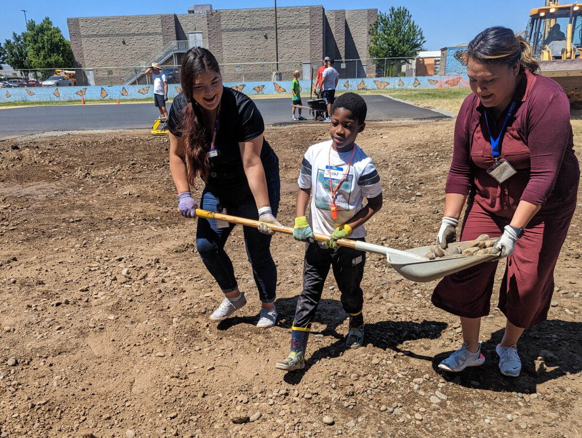 2 people help a student carry a shovel