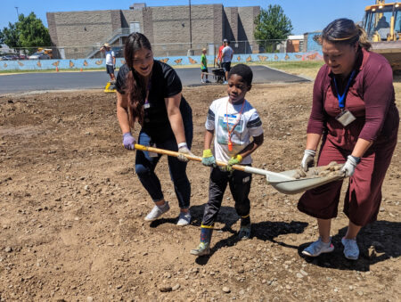 2 people help a student carry a shovel